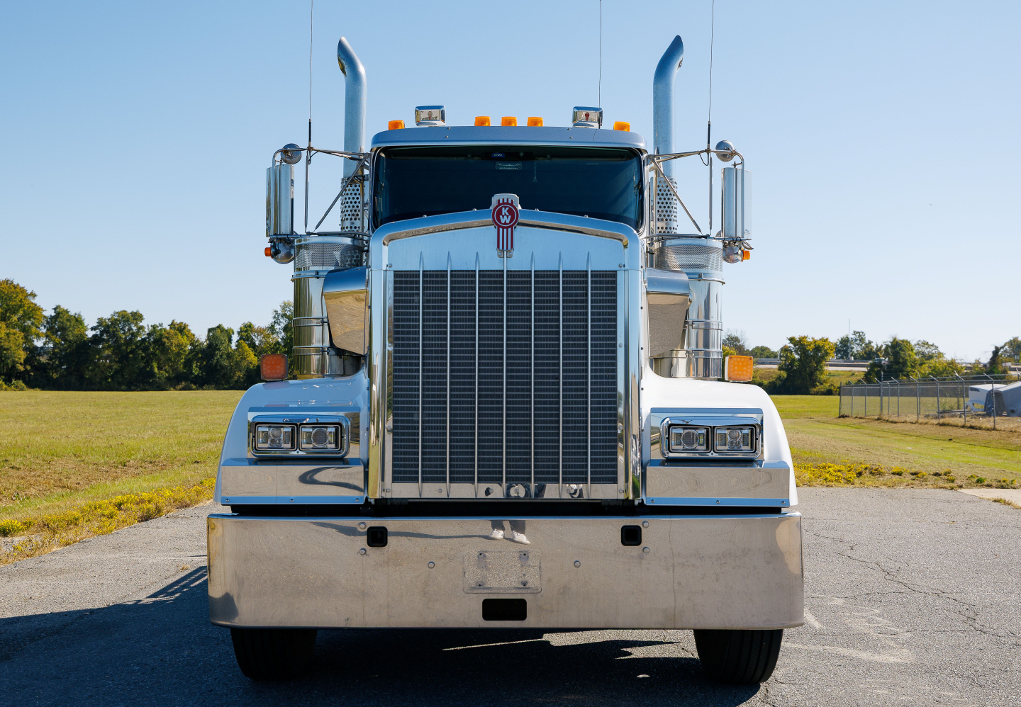 Kenworth W900L truck front view showing large chrome grille and bumper, dual air horns, stacked exhaust stacks, and clear windshield with mirrors.