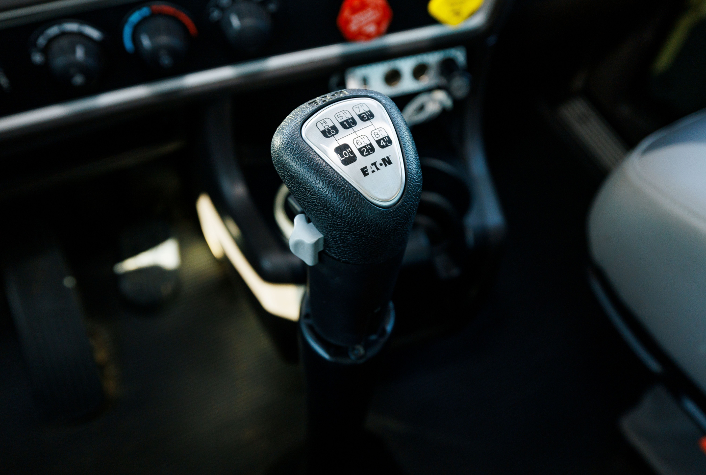 Kenworth truck gear shifter with white label showing gear positions; dashboard controls visible in background.