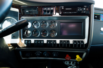 Dashboard view of a Kenworth truck cab showing multiple round gauges, a touchscreen, switches, and ignition area.