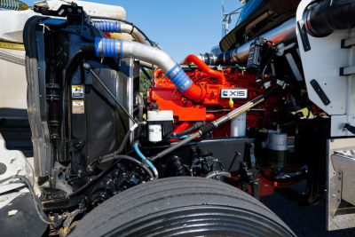 Kenworth W900L engine bay showing large red engine block with blue coolant hoses and black surrounding components.