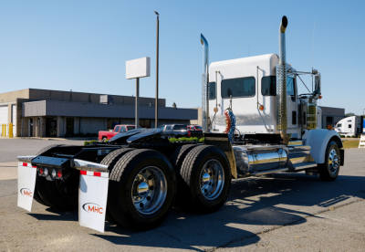 Kenworth W900L truck from rear three-quarter view showing dual rear axles and chrome fuel tanks.