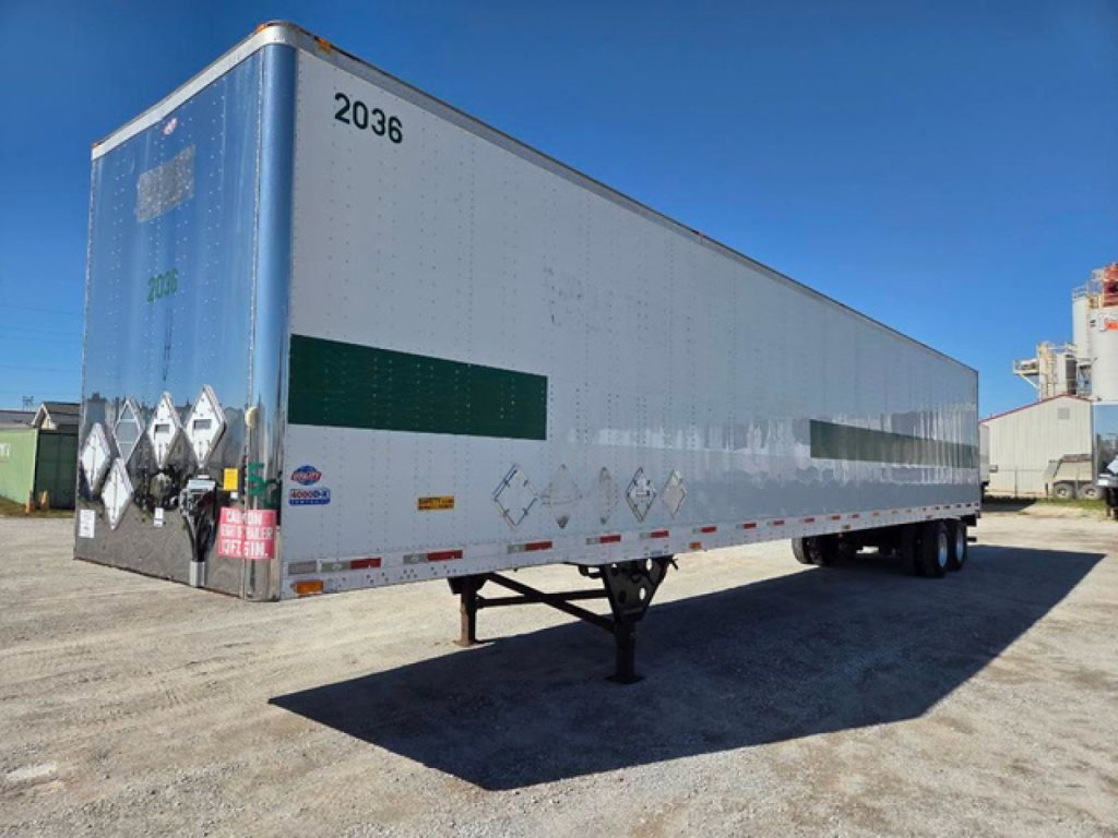 Trailer side view showing a white dry van trailer with a green rectangular panel, number 2036 on front corner, and landing gear in the foreground.