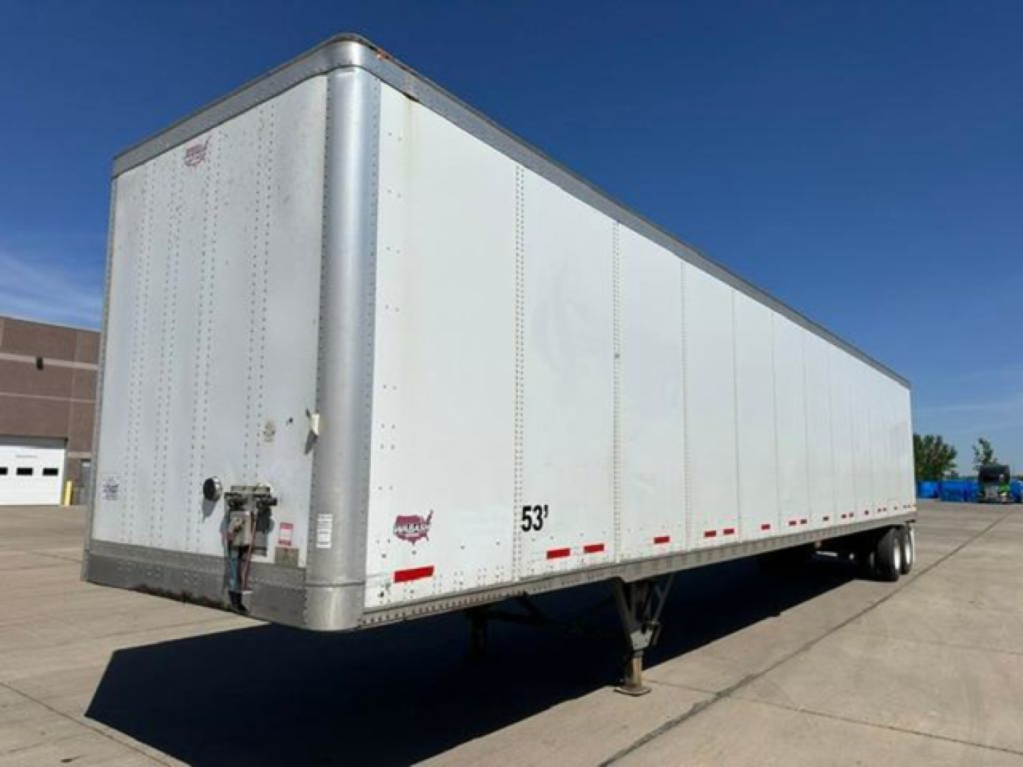 Flatbed trailer showing 53' length and a nose plate; side text includes 53' marker near front, reflective dots along lower edge, various riveted panels.
