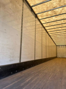 Interior of a trailer cargo area showing wooden floor, sidewalls with vertical rails, and ribbed ceiling.