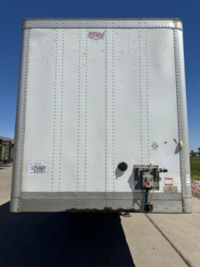 Back view of a white Wabash van trailer with a rear bumper and hitch, visible riveted panels and small stickers.
