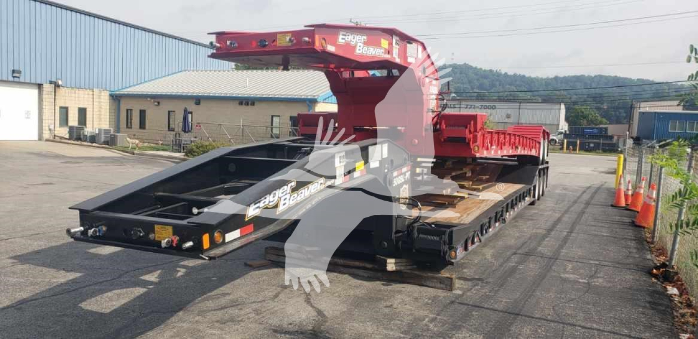 Lowboy trailer with red lifting deck and black main platform showing Eager Beaver branding and construction in a yard.