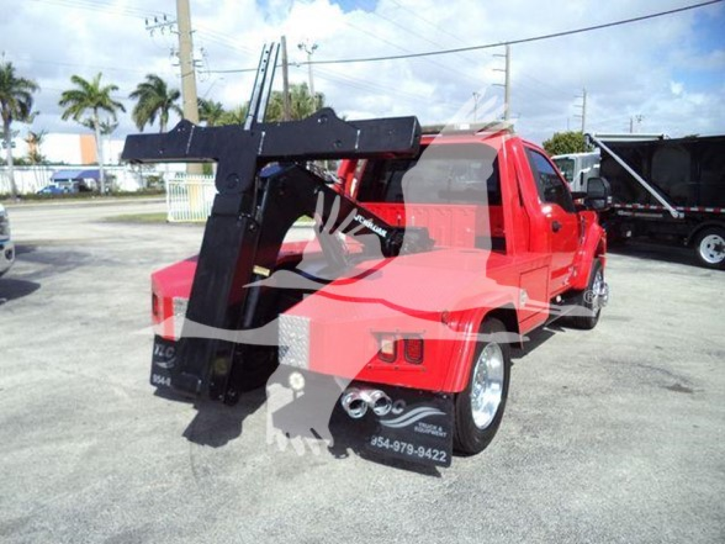 Ford F-450 tow truck with a large crane/winch apparatus mounted at the rear, red cab and chassis, black lifting arm, visible license plate area, sticker text on rear wheel well area.