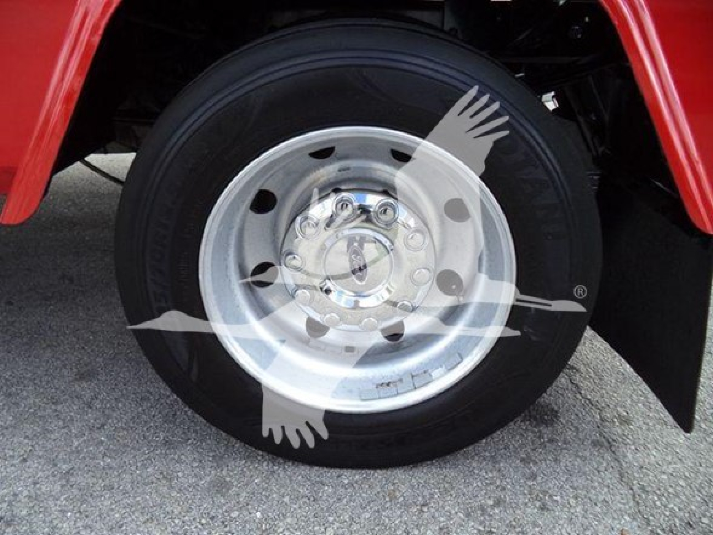 Wheel close-up on a Ford F-450 dually with a polished aluminum rim and black tire in a red fender area