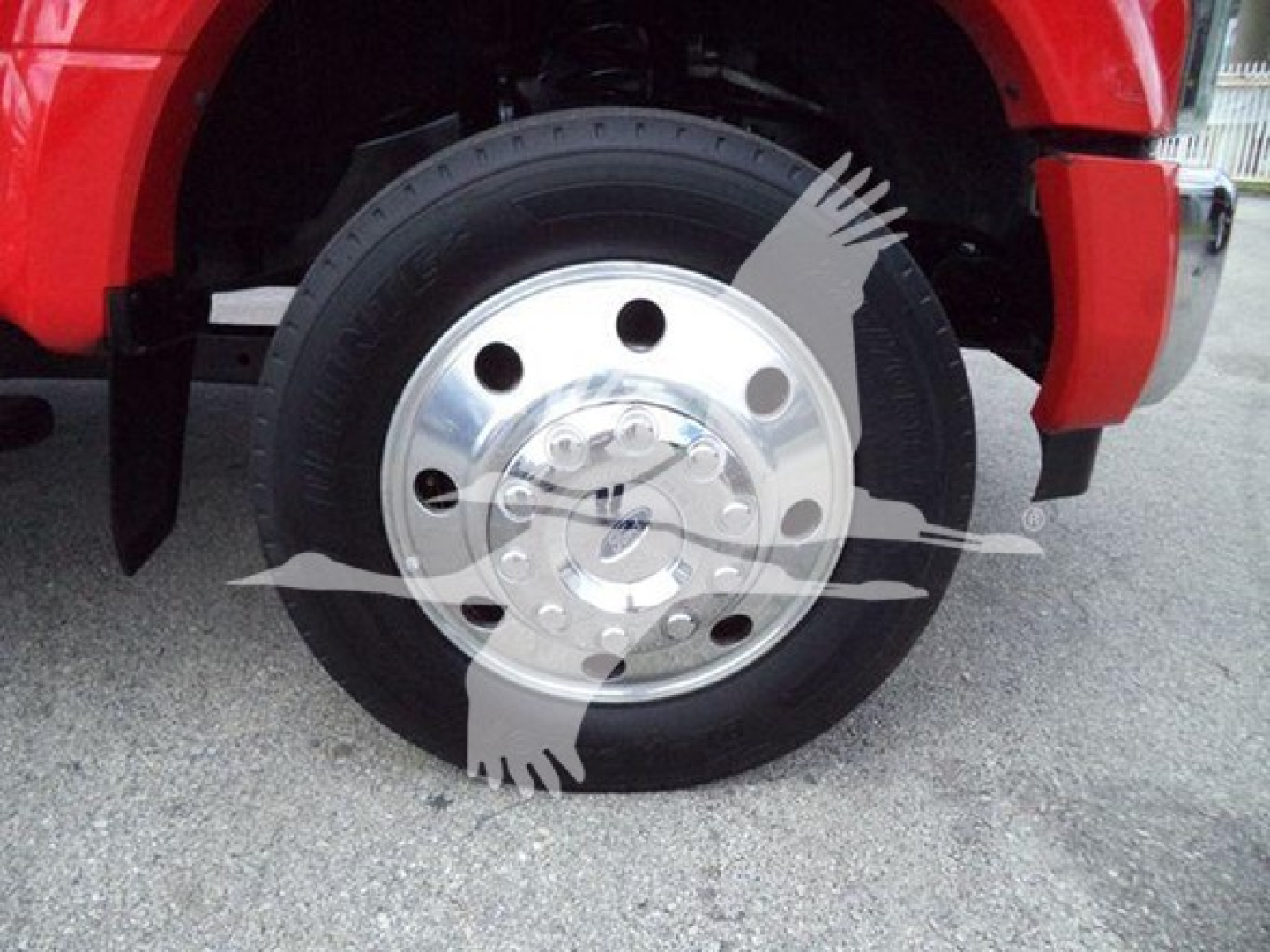 Wheel of a red Ford F-450 truck with a polished steel hubcap and black tire, partial fender visible.