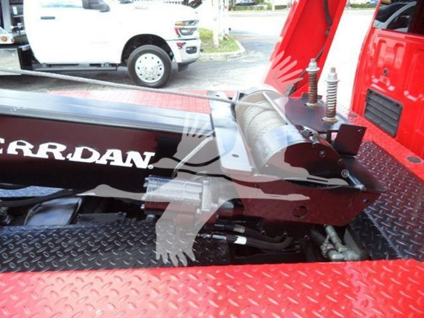 Ford F-450 winch apparatus mounted on a flatbed with red paint and diamond plate surface; visible components include hydraulic winch drum and mountingHardware.