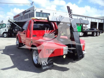 Ford F-450 tow service pickup with large winch arm attached in red color, front view, in a lot with other trucks and a building in background.