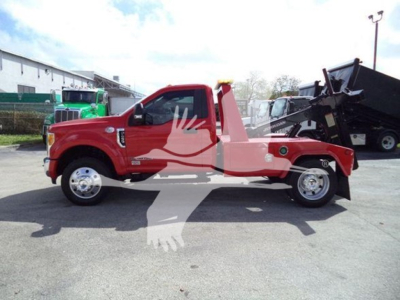 Ford F-450 tow truck side view showing winch equipment and red body with black industrial bed.