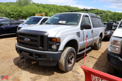 Ford F-250 Super Duty pickup truck in a salvage yard, white, with utility cap and black front grille, viewed from front-left side.