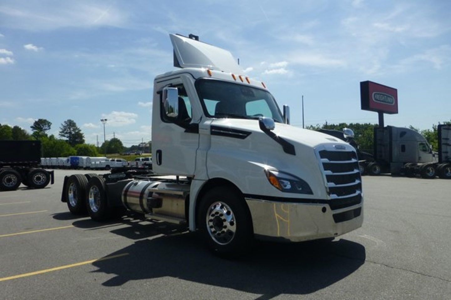 Truck cab exterior showing Freightliner Cascadia 126 with white cab, elevated exhaust, and front chrome bumper. Visible signage and lot in background.