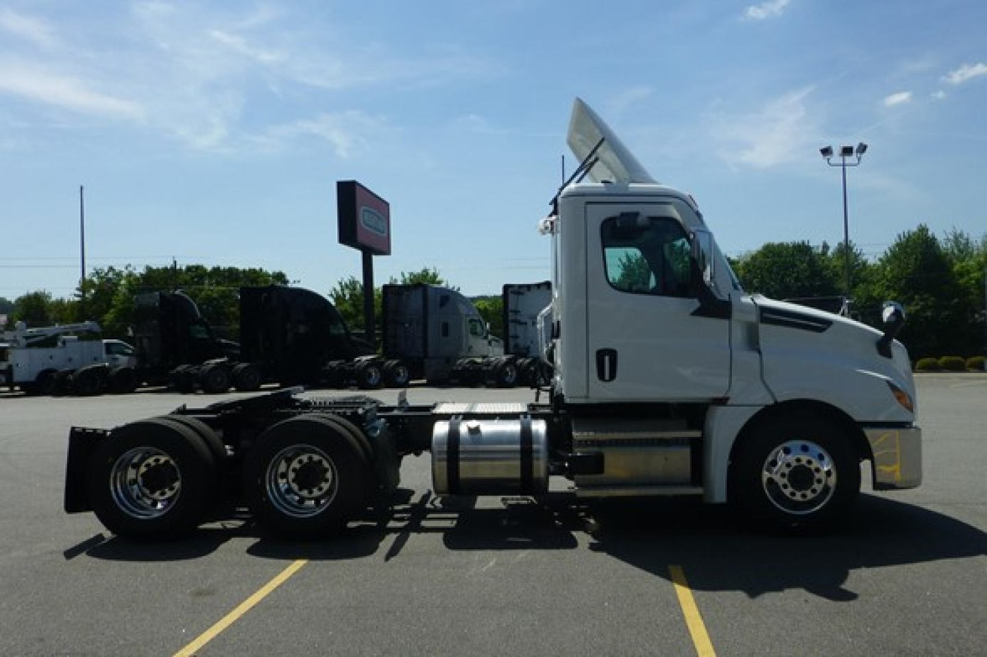 Truck tractor side view showing Freightliner Cascadia cab and chassis with empty trailer connection, white cab, dual rear axles, chrome fuel tanks, and sun visor on highway lot.