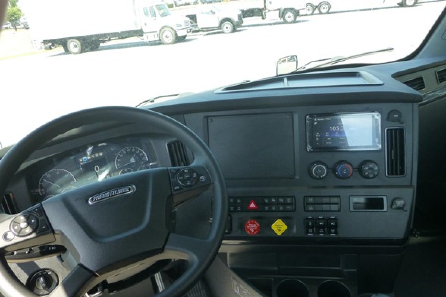 Freightliner Cascadia cab interior showing steering wheel, dashboard gauges, center console, and touchscreen display in a new truck.