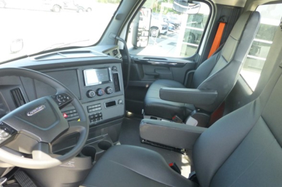 Truck cab interior showing steering wheel, dashboard, and driver seat of Freightliner Cascadia 126 cab with center console and touchscreen display.