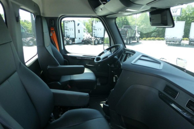 Truck cab interior showing steering wheel, dashboard, and driver seat with armrest; light gray/black plastics; windshield and side window visible.