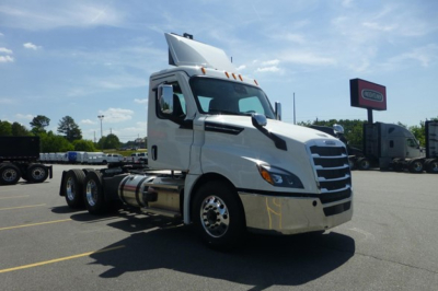 Truck cab exterior showing Freightliner Cascadia 126 with white cab, elevated exhaust, and front chrome bumper. Visible signage and lot in background.