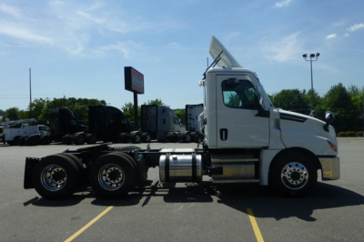 Truck tractor side view showing Freightliner Cascadia cab and chassis with empty trailer connection, white cab, dual rear axles, chrome fuel tanks, and sun visor on highway lot.