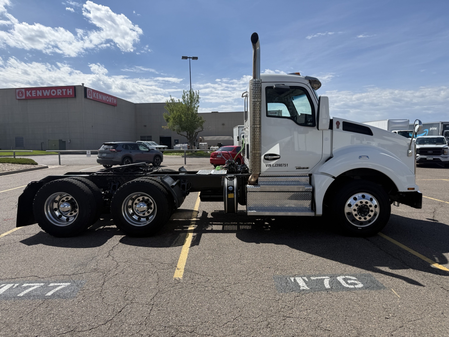 Kenworth T880 truck chassis side view with white cab, vertical exhaust, aluminum fuel tanks, and dual rear axles. Visible texts include Kenworth logos on building, VIN plate area, and wheel area.