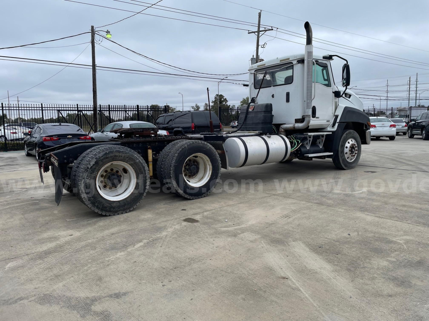 Truck chassis and cab of a Caterpillar CF7AA model in a used truck lot showing front cab and rear drive axles with fuel tanks and exhaust stack