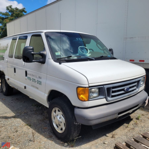 Ford E-Series van with text on door: 'SAWYERHILL MA' and phone number; front grille and headlights visible; white cargo van with side marker; background shows a trailer.