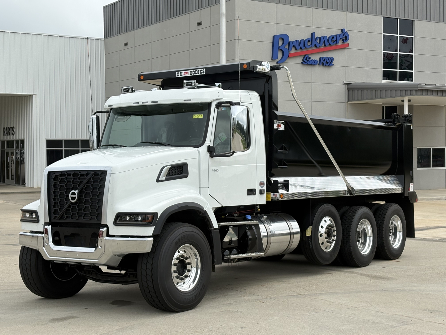 Volvo VHD84F300 dump truck in white with Brackner's dealership building in background.