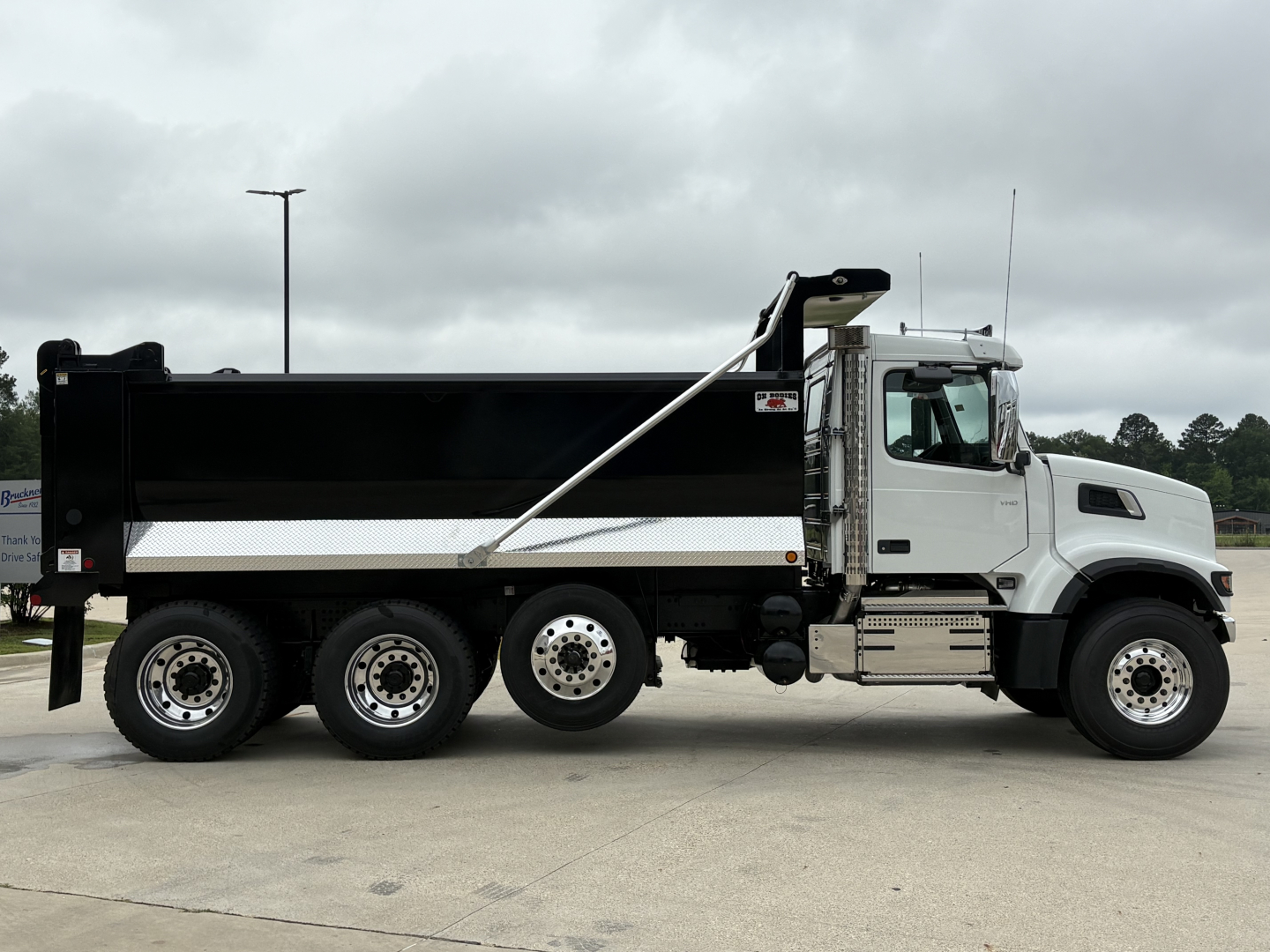 Volvo VHD84F300 dump truck side view showing large dump bed, white cab, black bed with chrome steps and aluminum side rails.