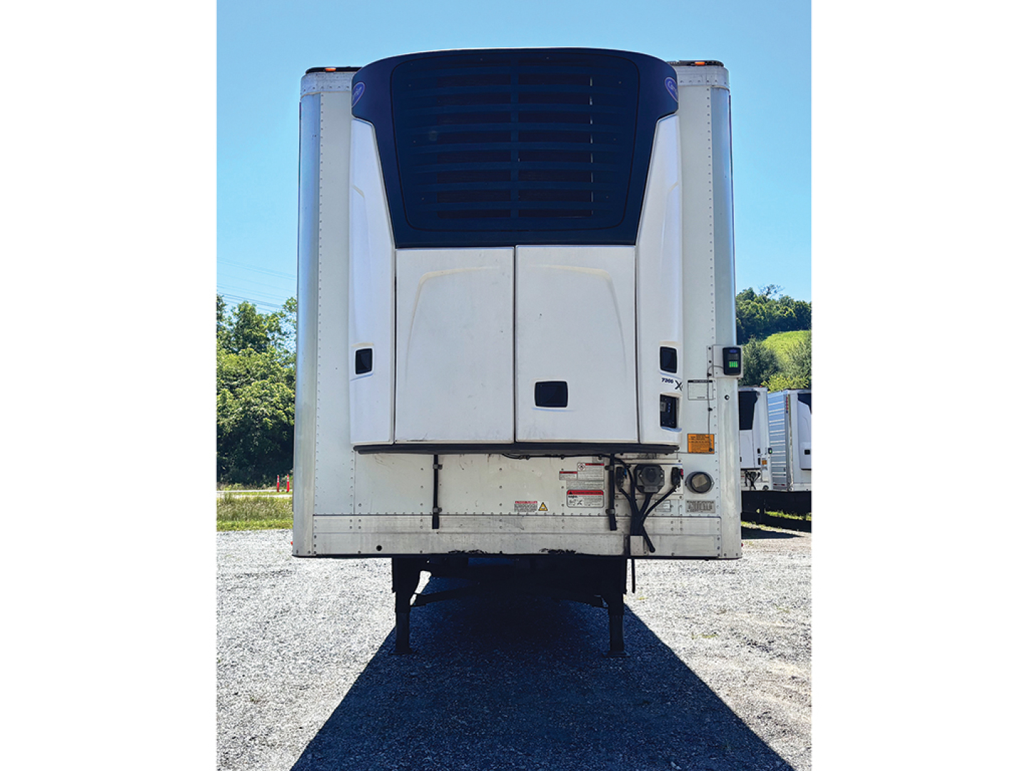 Rear view of a Utility 3000R trailer with Thermo King or similar refrigeration unit, white body with blue top section, two rear doors, elevated landing legs visible.
