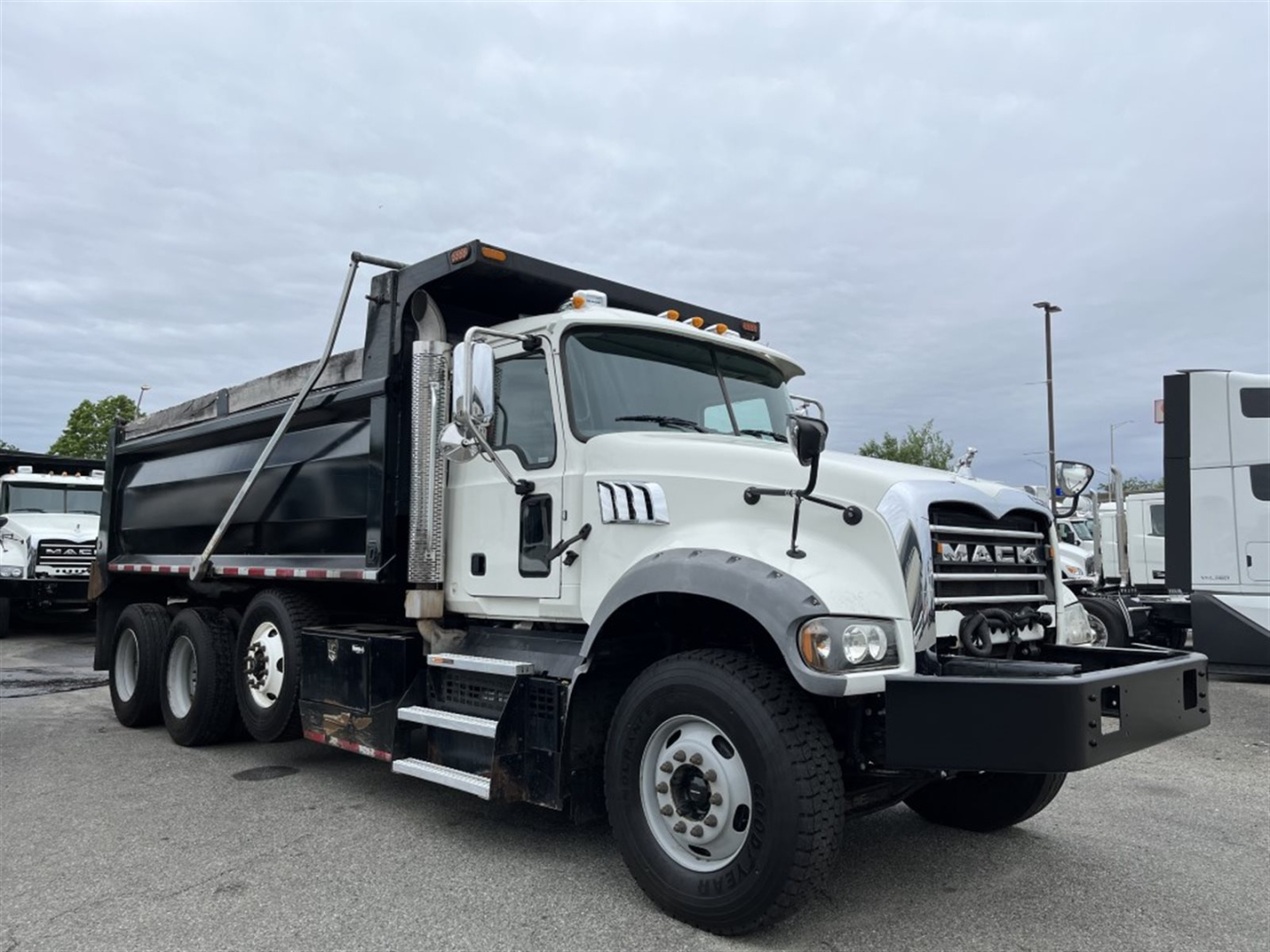 Dump truck showing 2023 Mack GR84F with white cab and black dump bed, side steps, grille, and front bumper; visible cab details and dual rear axles.