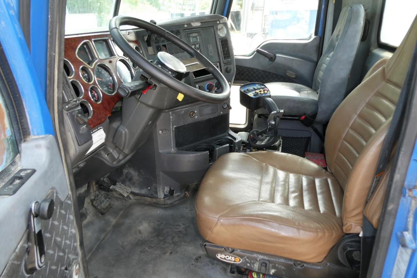 Truck cab interior with brown seat, steering wheel, dashboard, and gear shifter visible.