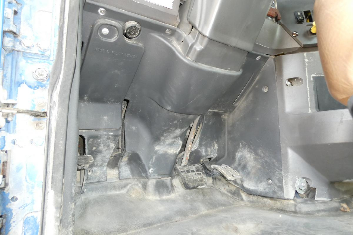 Cab floor and pedals area of a Mack CTP713 mixer truck showing accelerator, brake, and clutch pedals with surrounding plastic compartment and dusty floor mat.