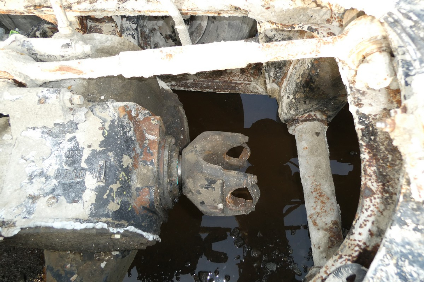 Mixer truck coupling with rusted hitch and mechanical components visible in a wet, muddy bay.