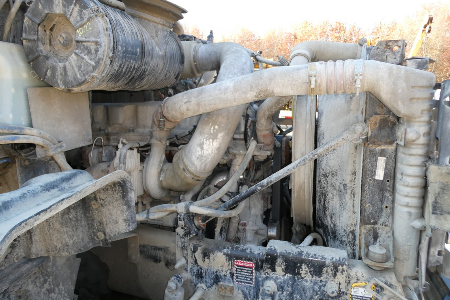 Mack mixer truck engine bay showing exposed hoses, radiator, and intercooler; engine components and grime visible under hood.