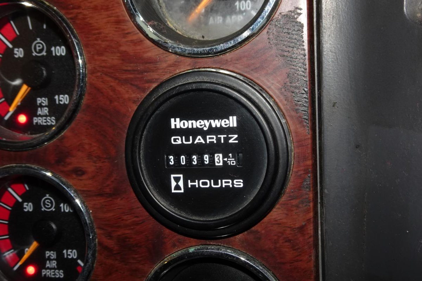 Mack mixer truck dashboard area with Honeywell Quartz hour meter showing 30393 hours and gauges around showing air pressure psi, wood-grain panel.