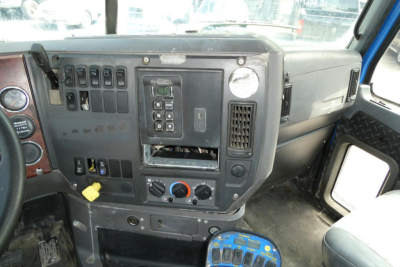 Dashboard and center console of a Mack mixer truck cab showing control panels, switches, gauges, and a circular blue device on the floor.