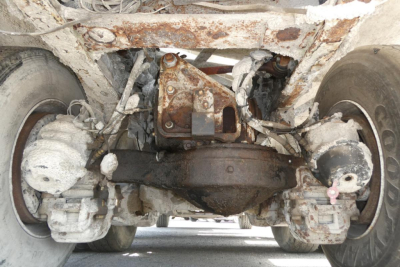 Underbody view of a concrete mixer truck axle and differential showing rusty housing and suspension components.