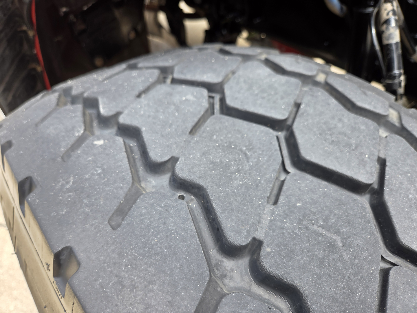 Tire tread close-up on Peterbilt 567 truck showing rugged lug pattern and wheel well. Partial cab components visible in background.