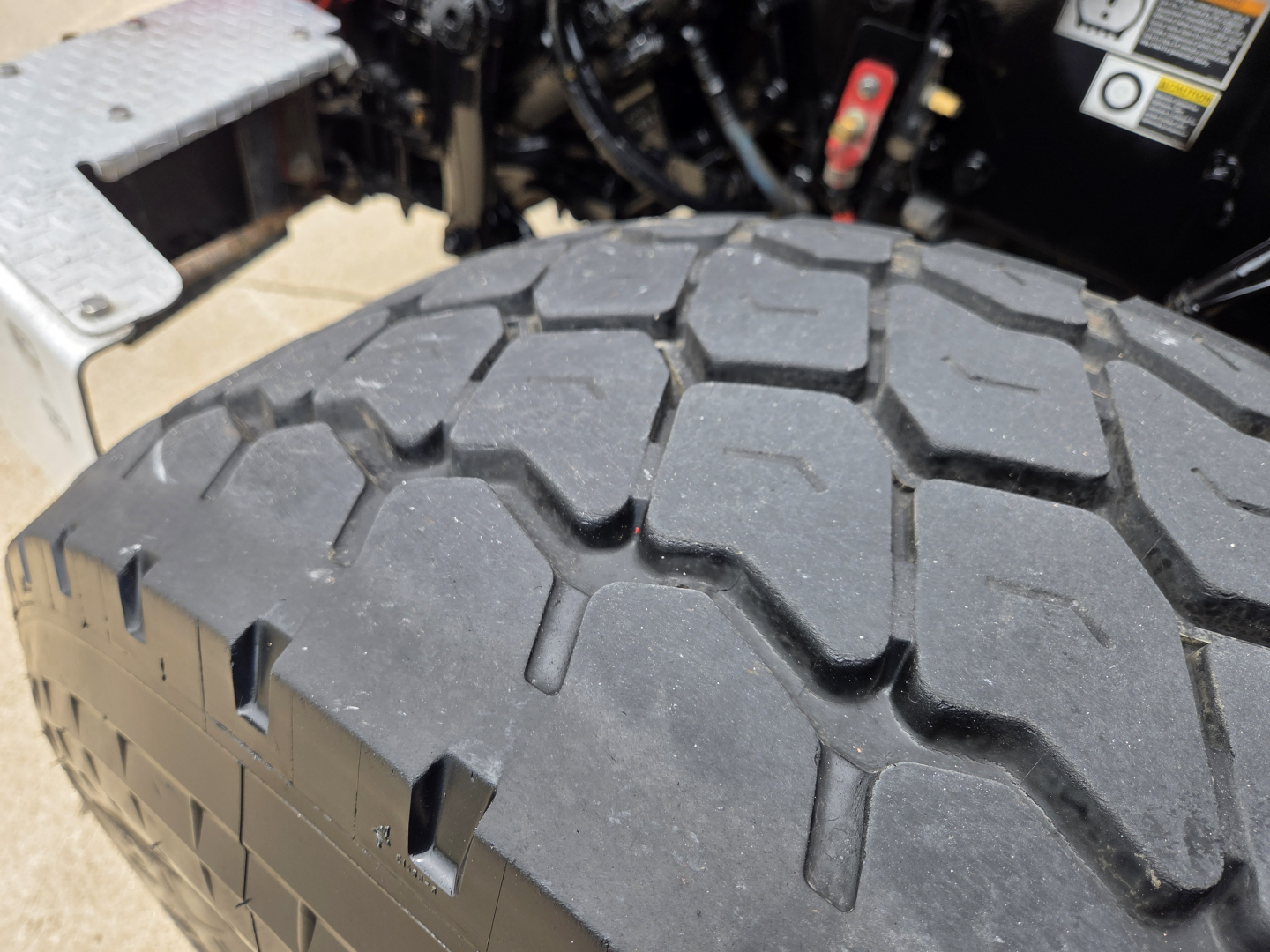 Peterbilt 567 wheel/tire close-up with tread pattern, part of a truck chassis visible in background including warning label and metal steps.