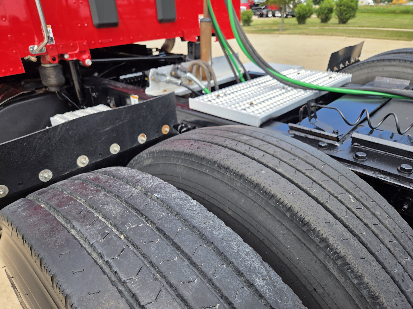 Peterbilt 567 truck chassis with dual rear axles and tires visible; metal steps and green hoses; part of the cab and frame in view.