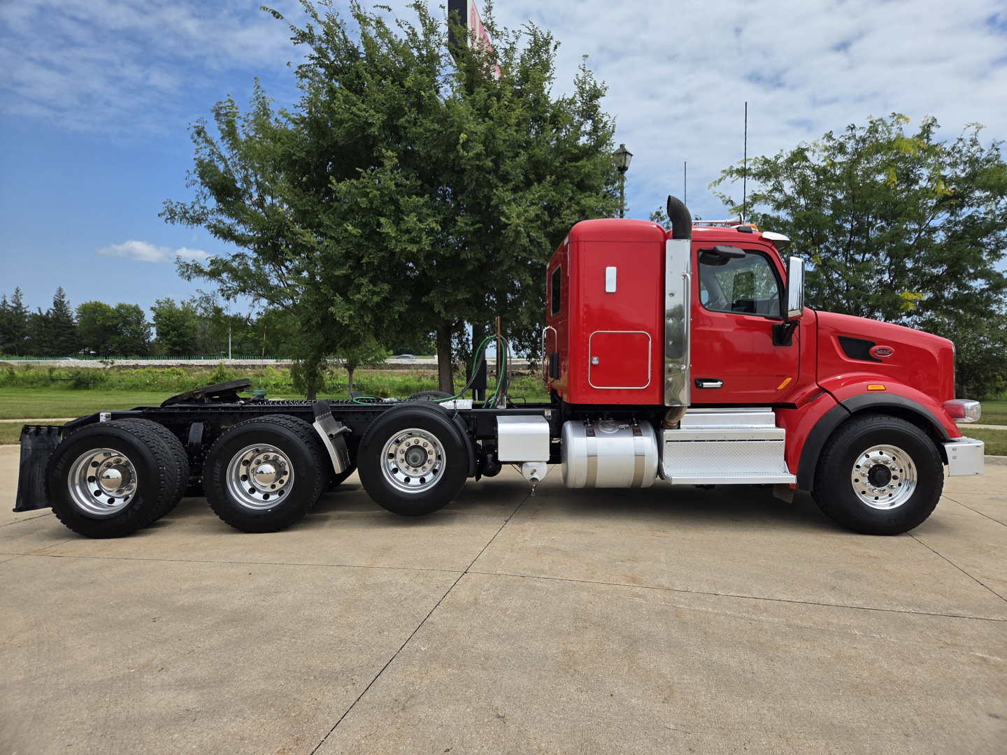 Peterbilt 567 truck side view showing red sleeper cab and dual rear axles with chrome fuel tanks