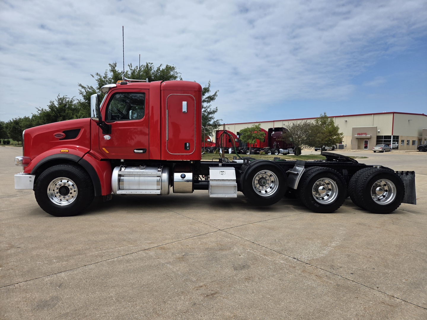 Peterbilt 567 truck side view showing red cab and multiple rear axles on a tractor-trailer chassis.
