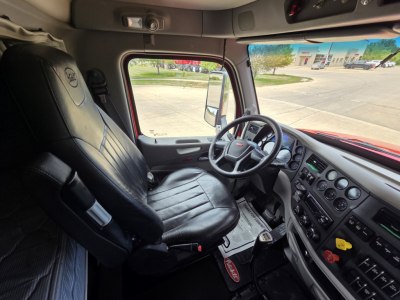 Truck interior front seats and dashboard of a 2020 Peterbilt 567 sleeper cab with steering wheel, instrument cluster, and control panels visible.