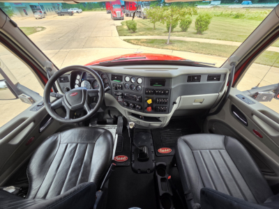 Peterbilt 567 cab interior showing steering wheel, dashboard, and driver seats with controls and center console.