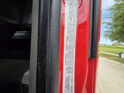 Vehicle door jamb label on a red Peterbilt showing VIN sticker with detailed specification table and adjacent exterior; part of cab area near the doorway.