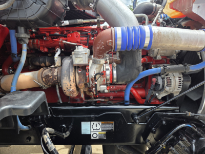 Peterbilt 567 engine bay showing red engine, blue coolant hose, turbocharger, and intake piping with metal clamps.