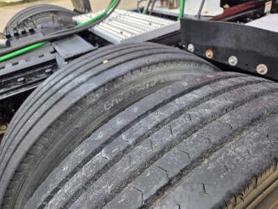 Dual rear tires on a Peterbilt truck showing tread and sidewall markings; visible parts include green and black wiring and metal mounting components.