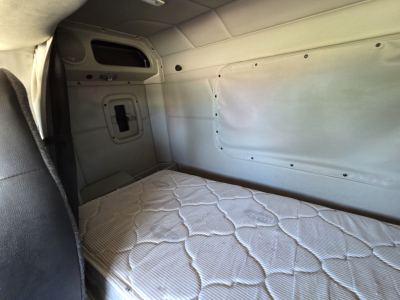 Peterbilt 567 sleeper cab interior with bed mattress, side paneling, and window cutout; light gray walls and sleeper cockpit area visible.