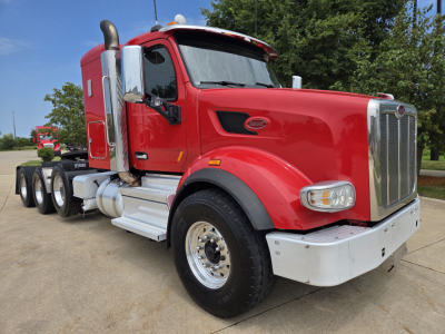 Peterbilt 567 truck in red parked outdoors, front three-quarter view, sleeper cab, chrome accents, dual rear axles, white bumper and steps.